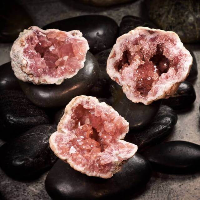 three raw pink amethyst crystals placed on smooth black stones