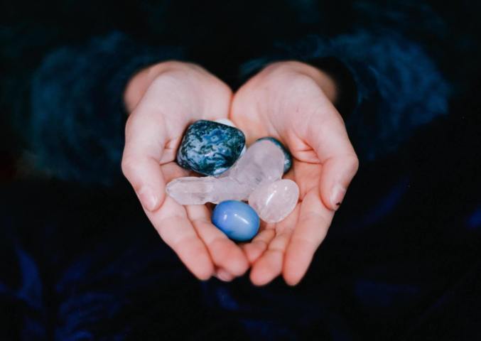 hands holding blue and white smooth stones and crystals black background