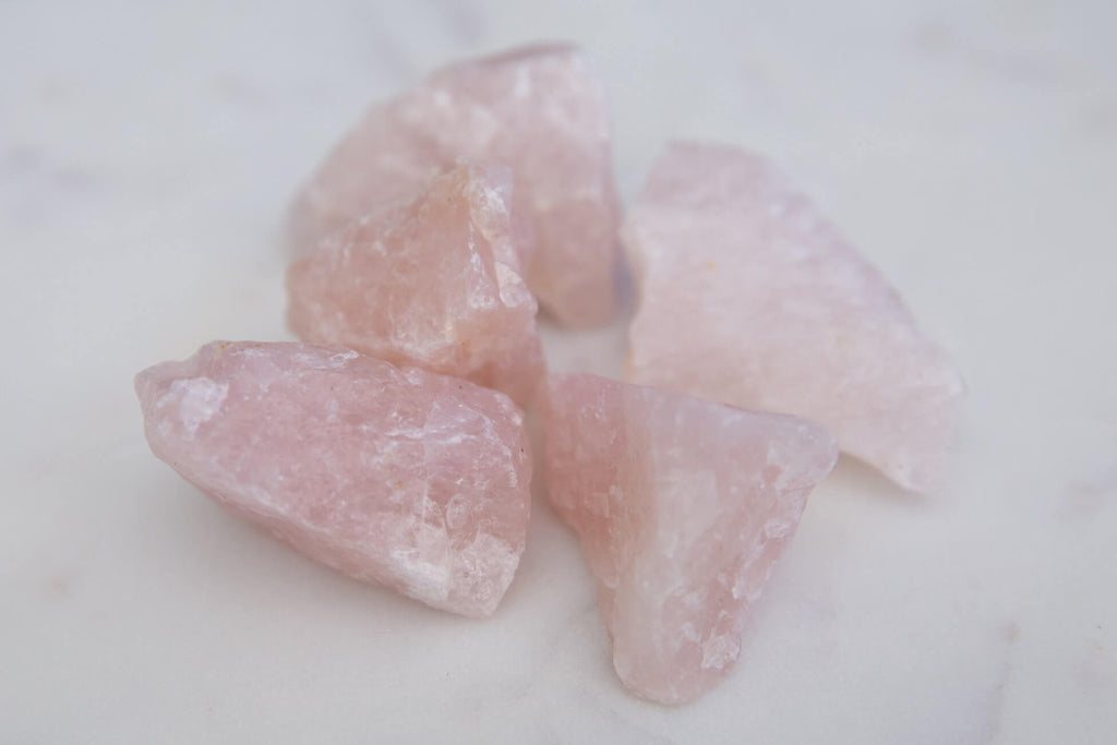 five pieces of unpolished pink crystal rock white background