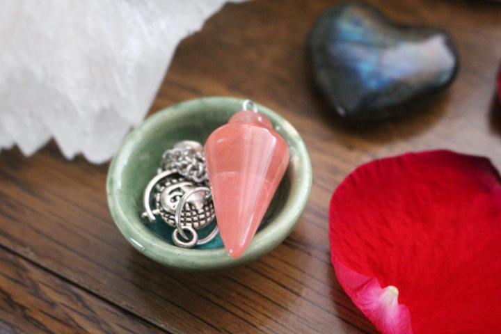 pink triangular smooth stone placed on tiny green plate pink petal on the side