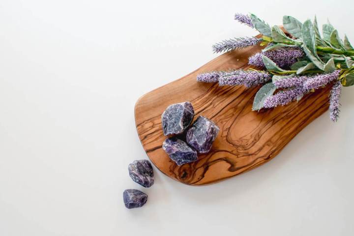 raw unpolished purple rocks placed on a wooden surface beside lavender flowers 