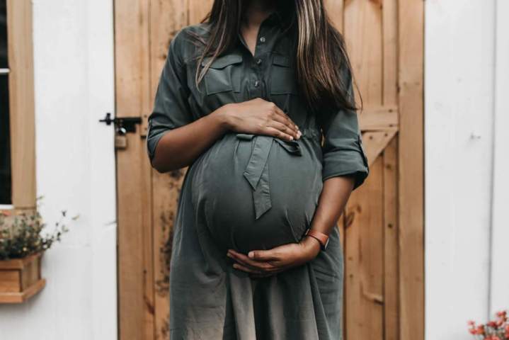 pregnant woman wearing gray dress holding her belly